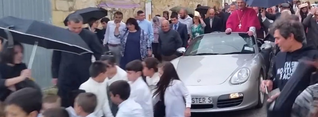 Десятки детей тащили по улице запряженный Porsche со священником
